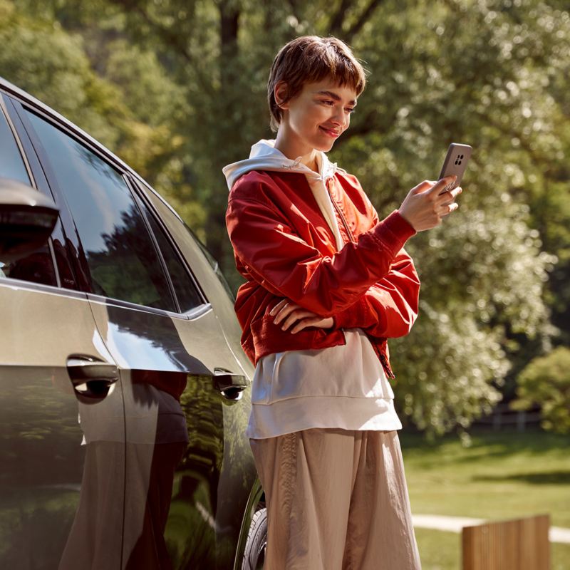 Une femme est devant une Volkswagen ID.3, un téléphone mobile dans la main