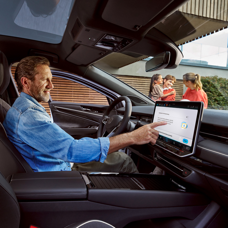 Mann sitzt in seinem VW ID.7 und berührt das Display, im Hintergrund eine Frau und zwei Kinder.