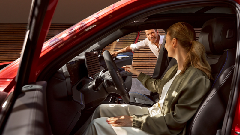 Blick von der Fahrerseite in einen roten Tiguan. EIne Frau sitzt auf dem Fahrersitz, ein Mann schaut durch die geöffnete Beifahrertür herein.