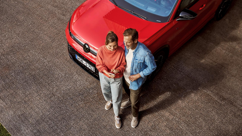 Pareja de pie delante de un Tiguan mirando el teléfono móvil