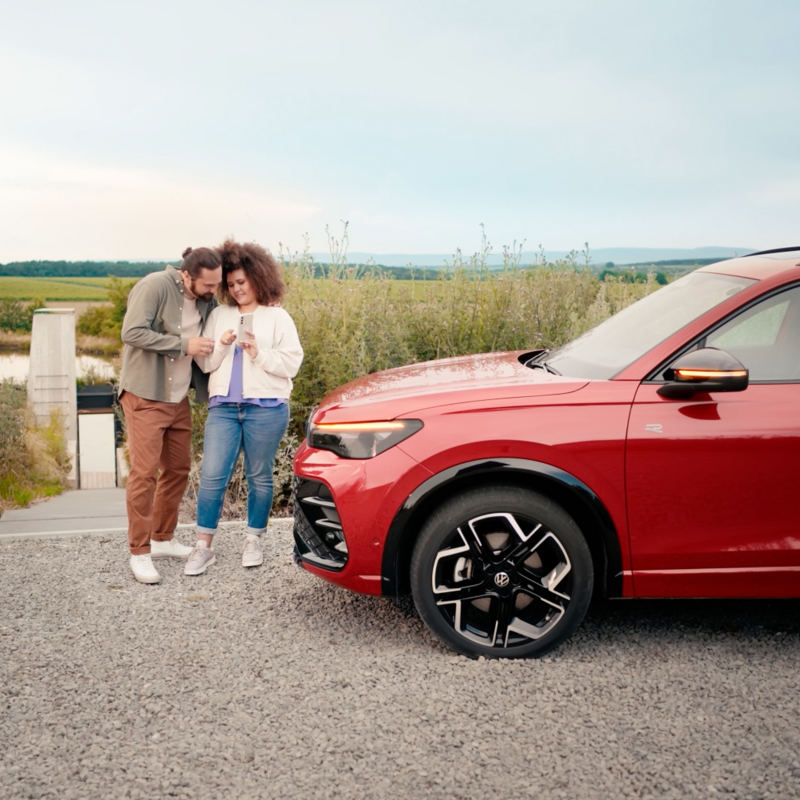 Une femme et un homme se tiennent devant leur Volkswagen et regardent leur smartphone.