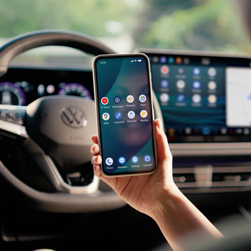 Person behind the wheel of a Volkswagen holding a smartphone.