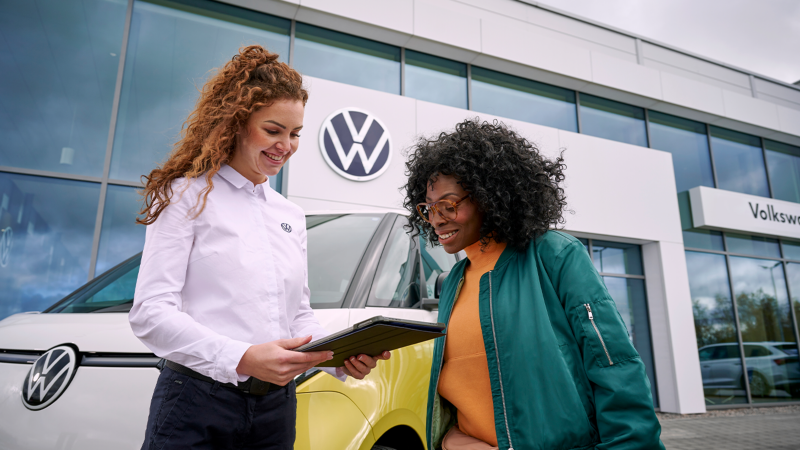 Représentante VW aidant une cliente devant une concession Volkswagen.