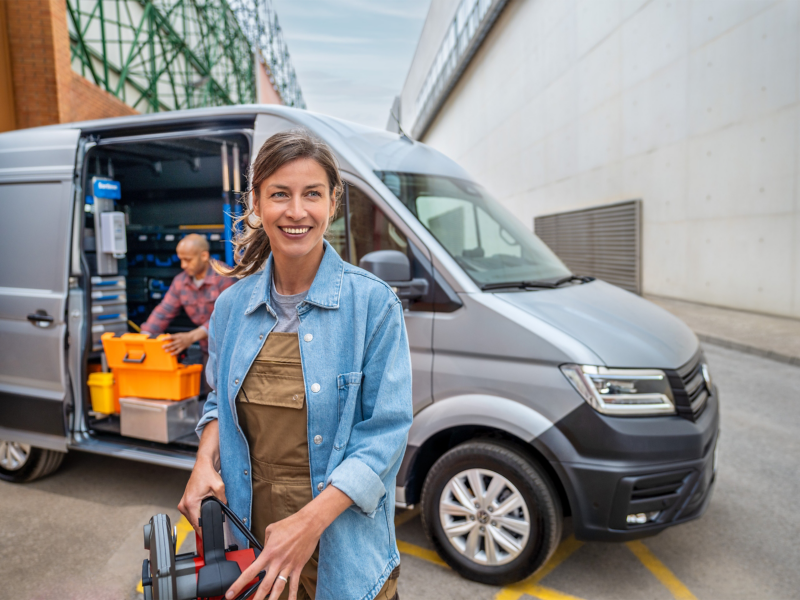 Eine Handwerkerin steht vor einem VW Crafter mit offener Schiebetür in einem Industriegebiet