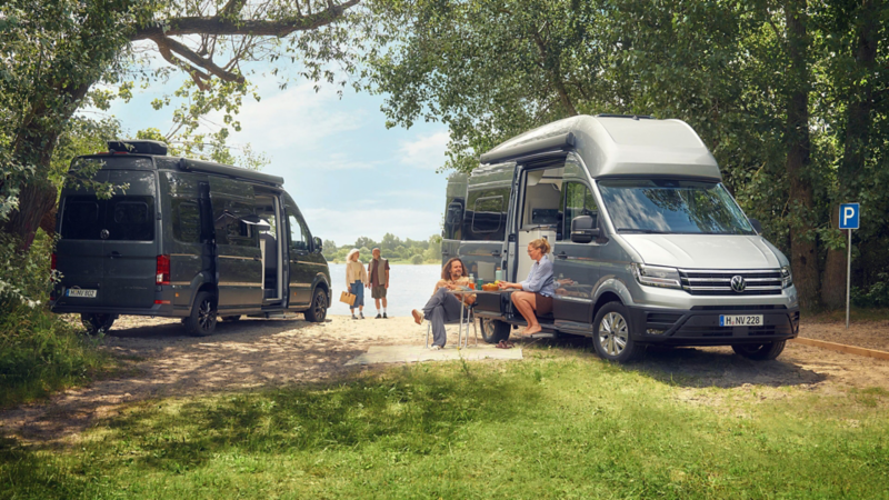 Zwei Pärchen und ihre VW California in einer idyllischen Seenlandschaft.