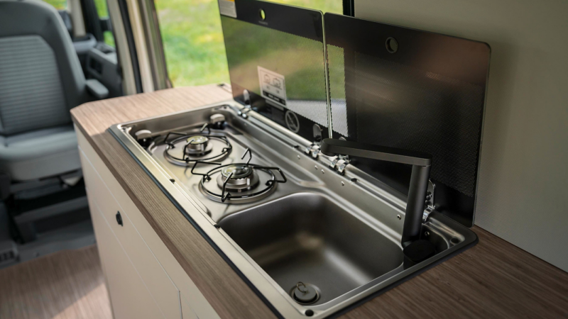 A gas powered hob with a drawer open underneath displaying utensils