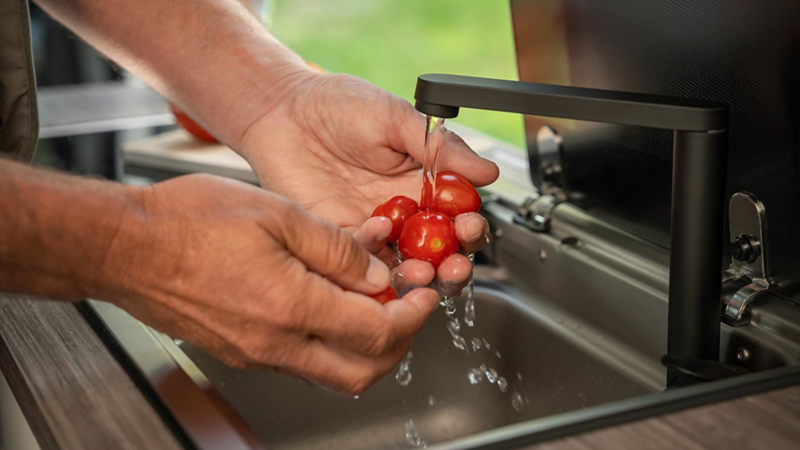 Nahaufnahme von Händen, die frische Cocktailtomaten in der Spüle waschen.