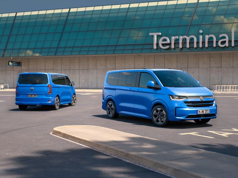 Två blåa Volkswagen Caravelle minibuss utanför en flygterminal