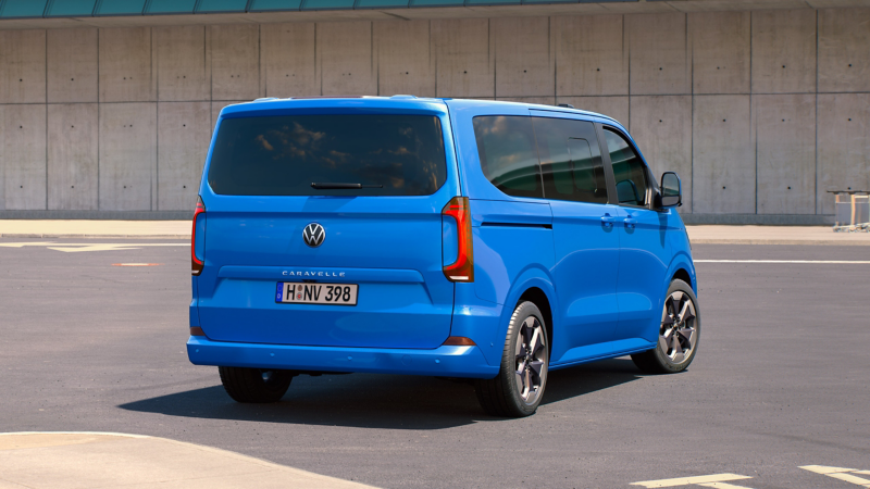 En blå VW Caravelle 9-sits minibuss bakifrån.