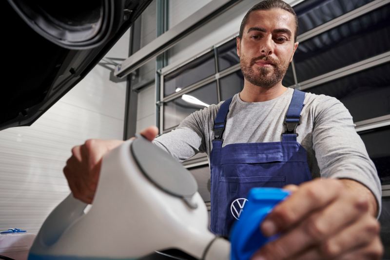 Een Volkswagen werknemer giet koelvloeistof in een Volkswagen auto