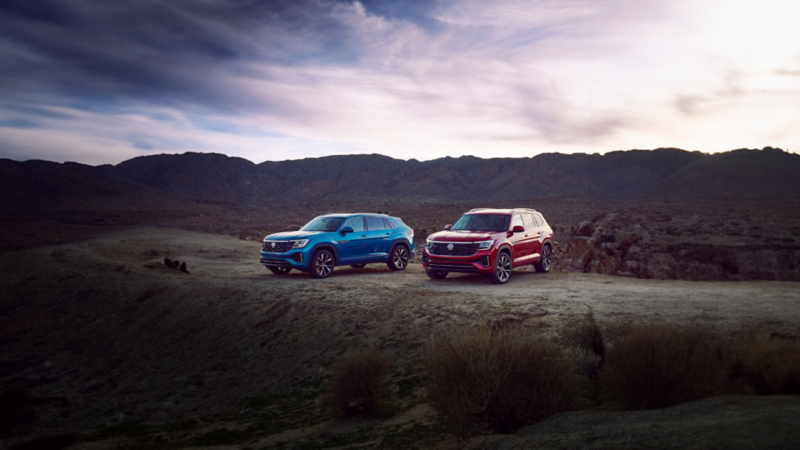 The Kingfisher Blue Metallic 2024 Volkswagen Atlas Cross Sport parked near the 2024 Aurora Red Chroma Atlas in the desert.