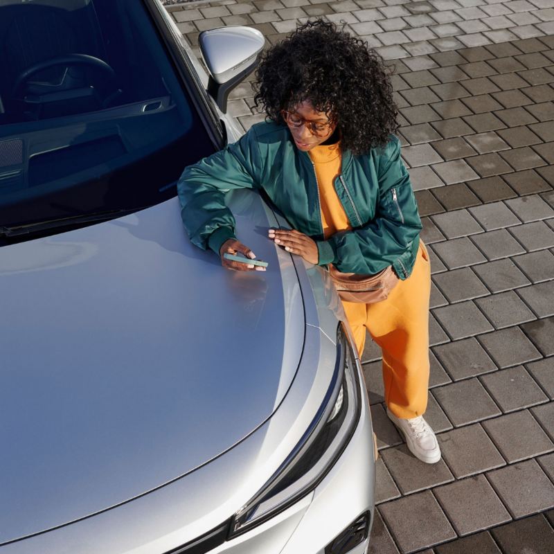 Une femme regarde son téléphone mobile en touchant le capot de sa voiture.