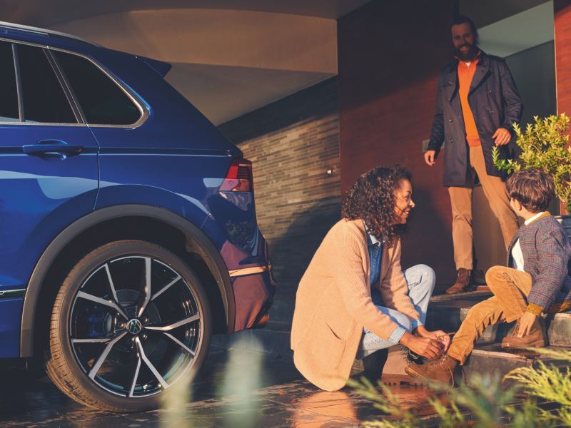 Une femme aide un garçon à attacher son soulier à côté d’un VUS Volkswagen bleu métallique.