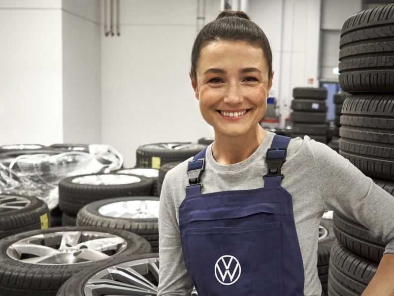 A smiling Volkswagen technician in the garage with a lot of tires on the background