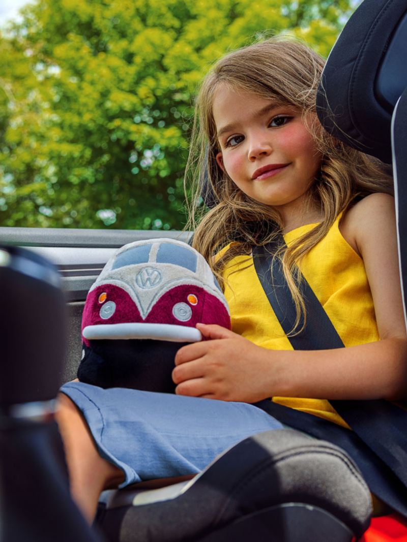A small girl sitting in the kid’s chair in the car and holding a Volkswagen toy in her hand