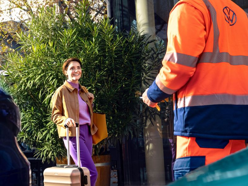 A woman with a luggage smiling towards a man in the Volkswagen uniform