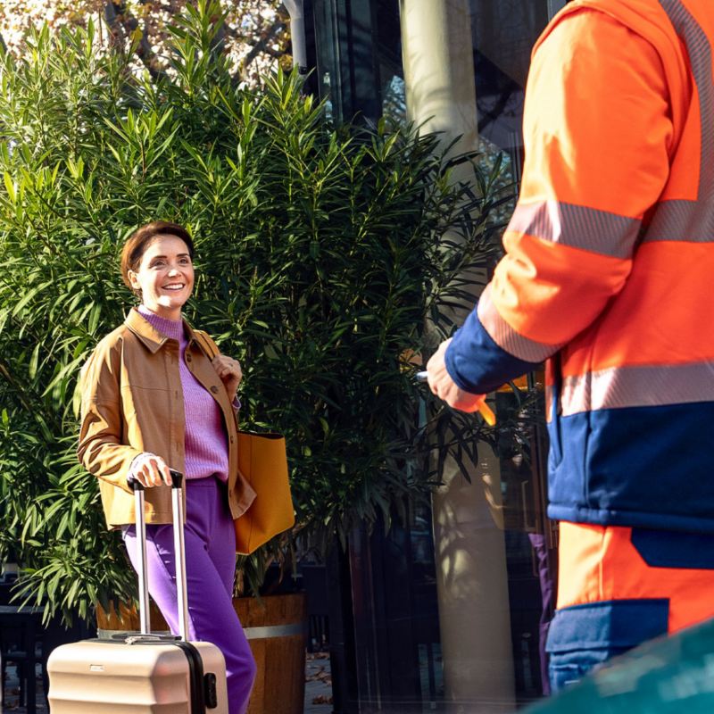 A woman with a luggage smiling towards a man in the Volkswagen uniform