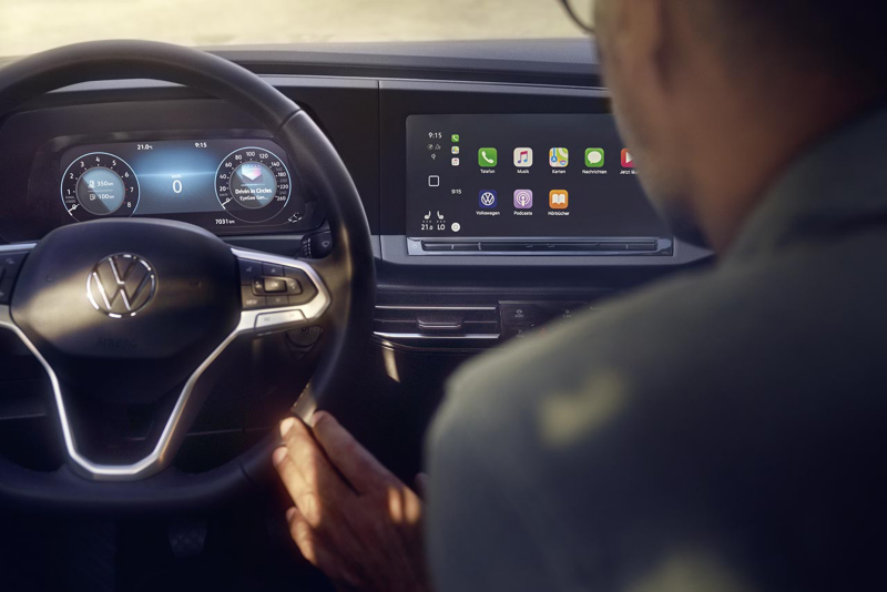 Gros plan sur le poste de conduite d'une Volkswagen Caddy montrant le volant multifonction, le tableau de bord numérique et l'écran central d'infodivertissement affichant des applications.