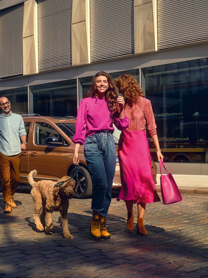 A Man passing by Volkswagen caddy along with two Women and a dog