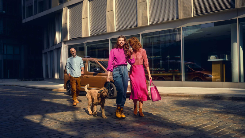 A Man passing by Volkswagen caddy along with two Women and a dog