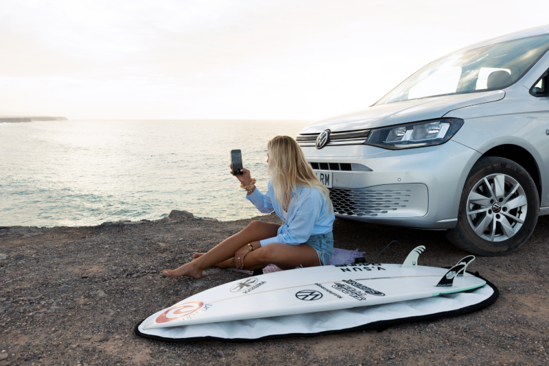 Una mujer apoyada en el VW Caddy aparcado en una playa.