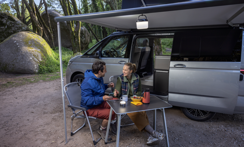 Dos personas junto al VW Nuevo California, con su mesa plegable exterior.