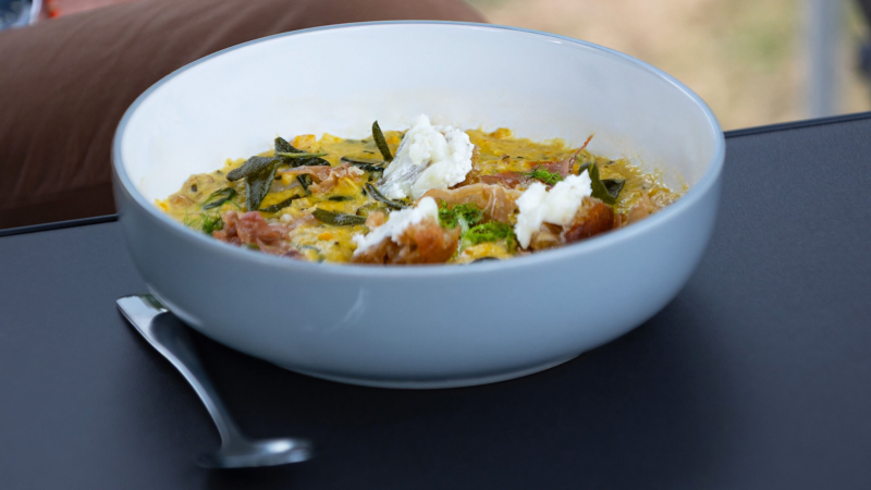 White bowl filled with a creamy risotto topped with herbs and cheese on a grey table.