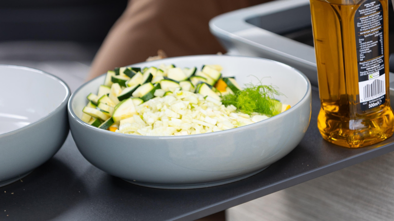 Chopped courgette in a bowl next to a bottle of olive oil on a countertop.