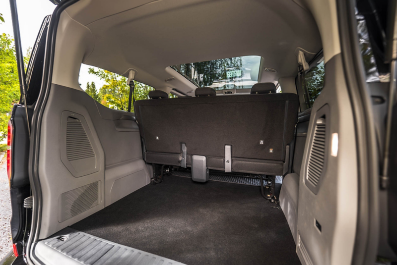 The VW Caravelle is parked in a meadow with four people standing behind it.