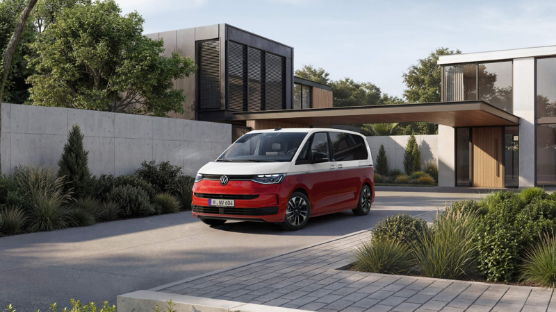 A red and white Volkswagen minivan is parked in front of a modern house with large windows and minimalistic landscaping, conveying a sleek, contemporary vibe.