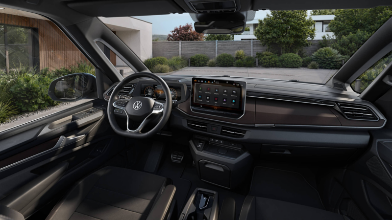 Modern car interior featuring a sleek dashboard, large touchscreen, and steering wheel with logo. Outside, a driveway and foliage are visible. Calm ambiance.