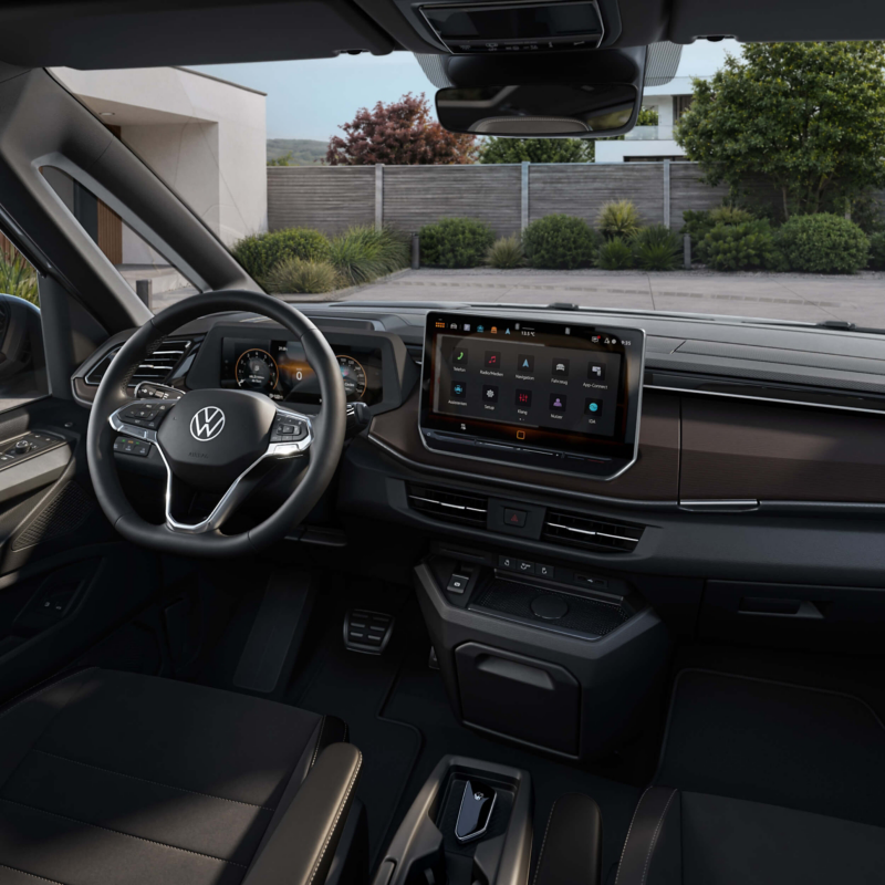 Modern car interior showcasing a sleek dashboard with a large digital display and multifunction steering wheel. Bright, calm exterior view outside.
