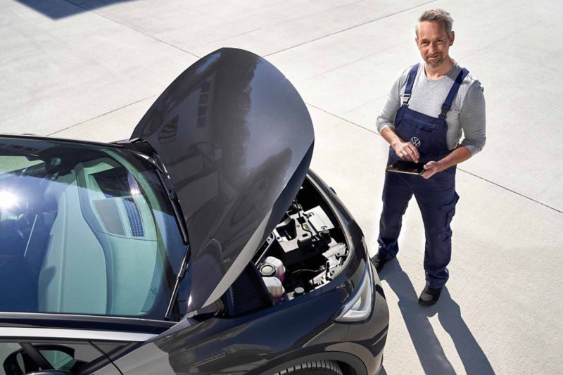Ripresa di un esperto Volkswagen mentre tiene in mano un tablet per eseguire un'opera di manutenzione di un veicolo.