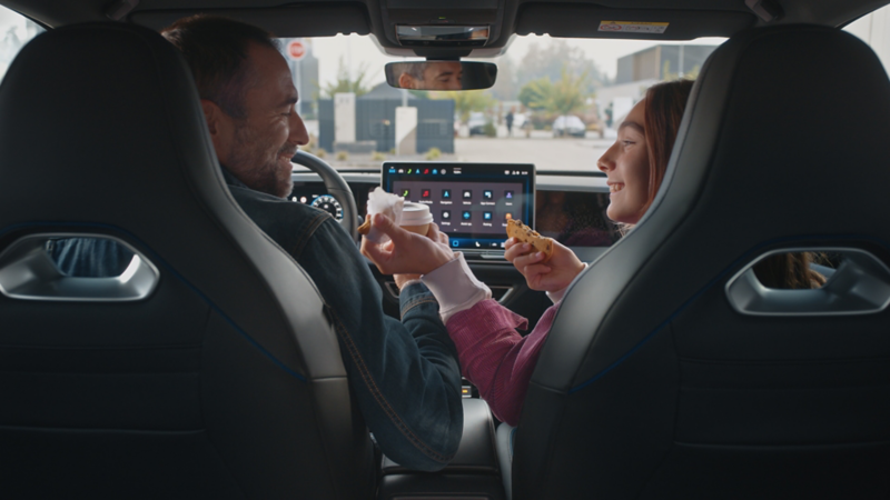 Driver and passenger using Volkswagen infotainment system while eating snacks inside vehicle.