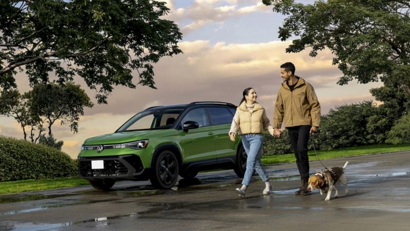 Un couple promenant son chien près d'un Volkswagen Taos 2025 vert garé dehors.