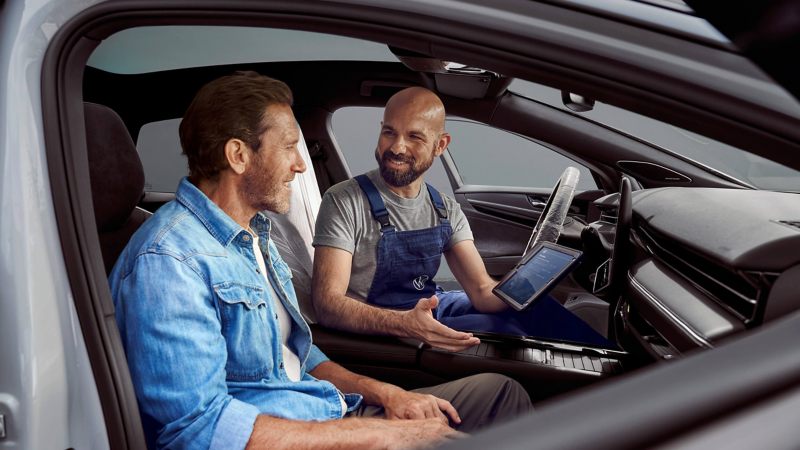 Photo showing a man talking to a VW technician in the cockpit of a VW van. 