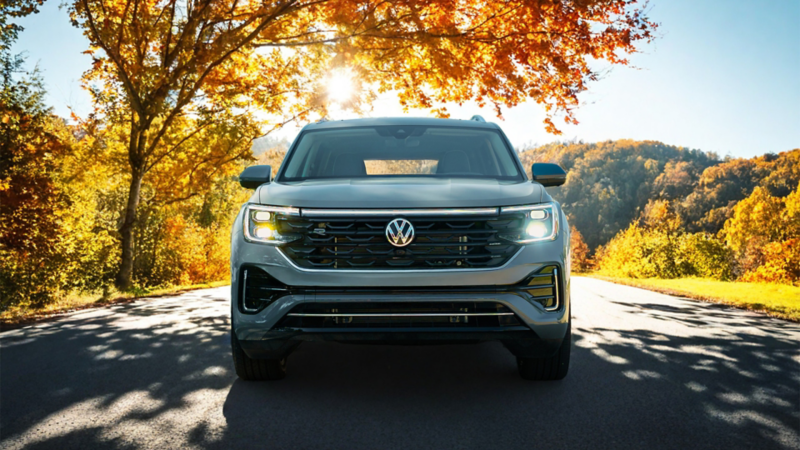 Front view of a silver SUV on a tree-lined road during autumn, with sunlight shining through colorful leaves, emphasizing bold design and seasonal scenery.