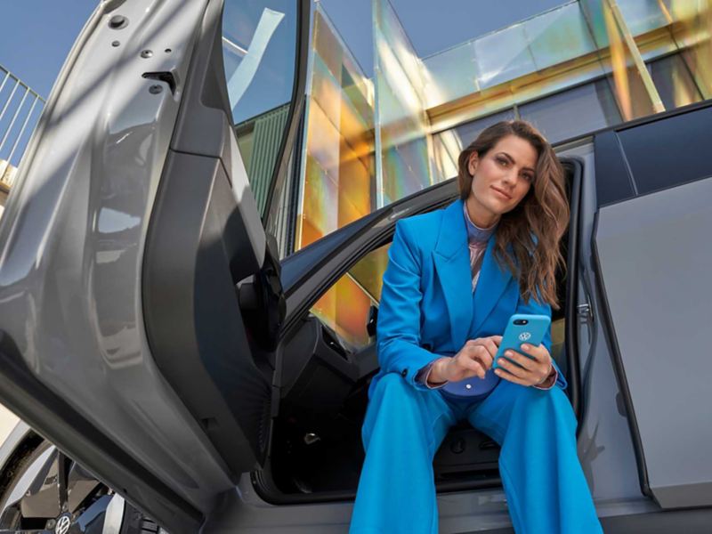 Una donna siede su una vettura con la portiera aperta, sullo sfondo un palazzo moderno.