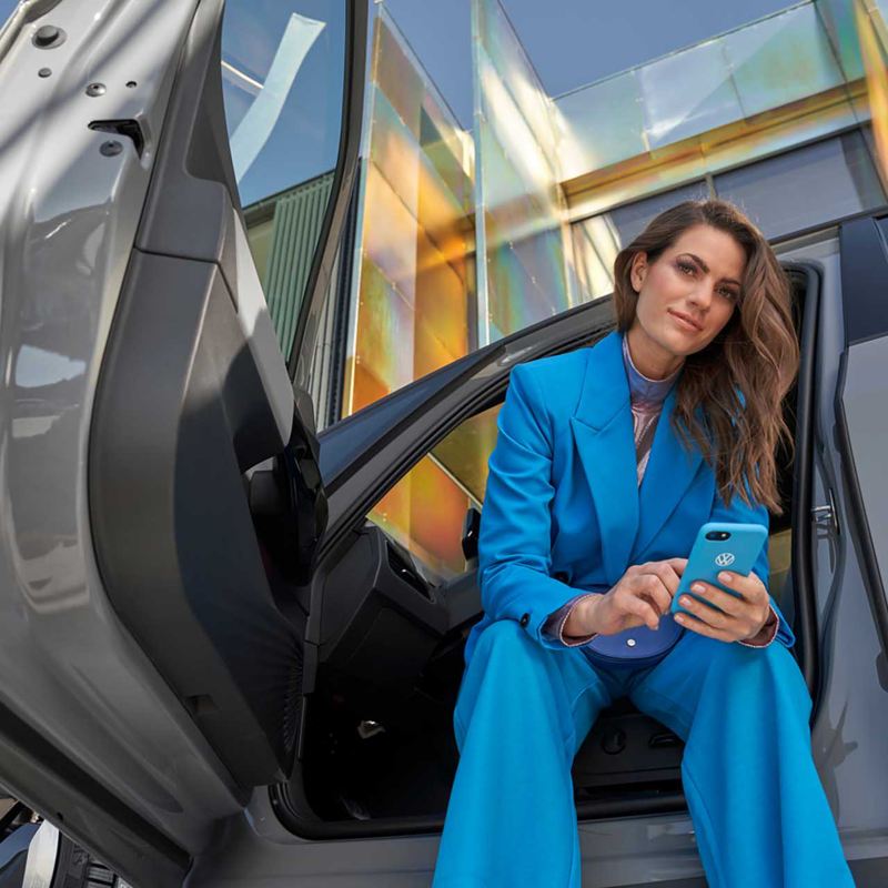 Una donna siede su una vettura con la portiera aperta, sullo sfondo un palazzo moderno.
