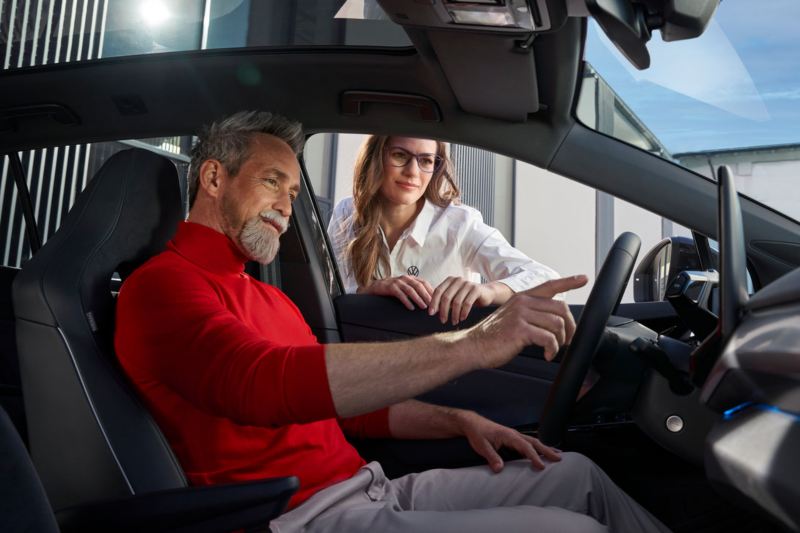 Una consulente Volkswagen assiste un uomo a bordo dell'auto che indica il sistema di infotainment.