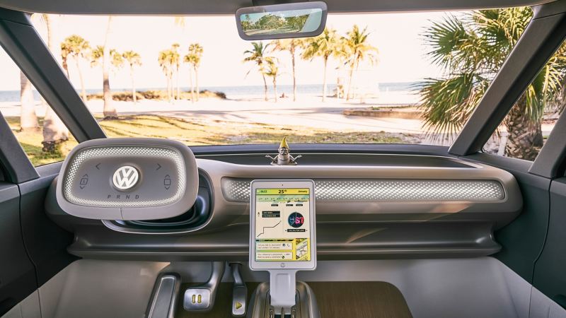 The interior of the Volkswagen I.D. BUZZ is shown with the steering wheel, the infotainment system and views of the beach through the windshield.