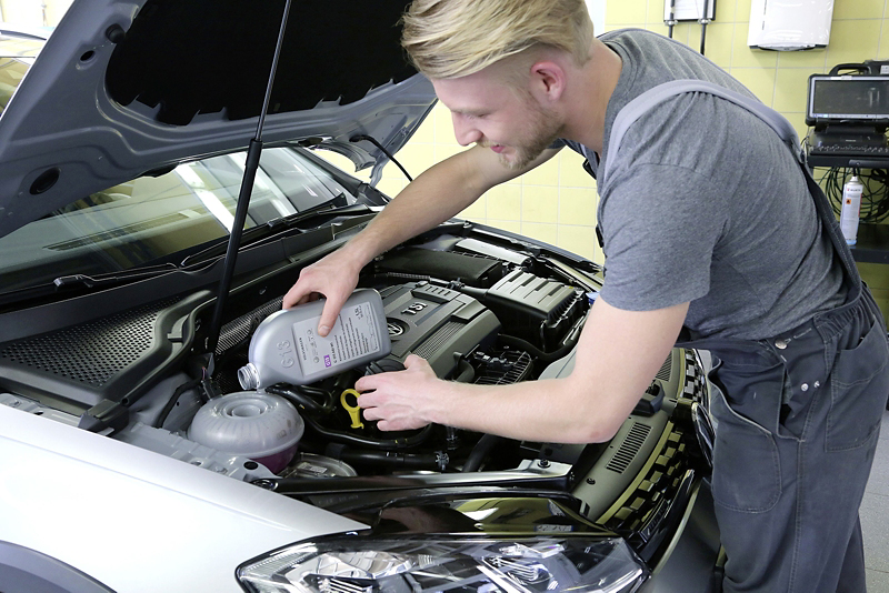 En man fyller på olja i en bil med öppen motorhuv