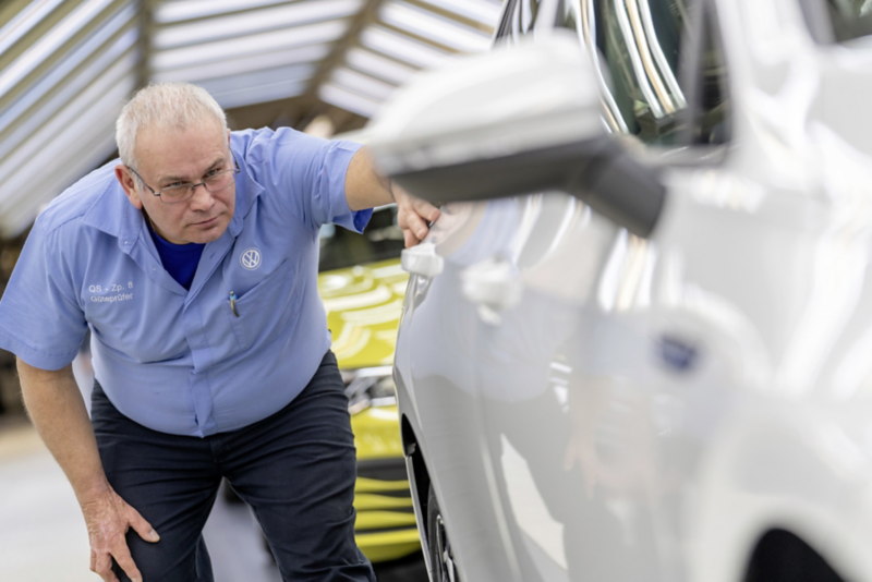 Volkswagen quality assurance employee inspecting the paintwork of a vehicle