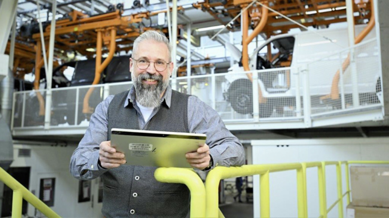 Mitarbeiter mit einem Tablet Computer in einer Produktionshalle mit Fahrzeugen im Hintergrund