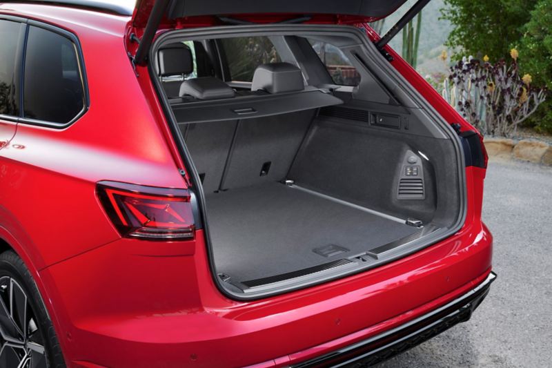 A man and a woman walk towards a VW Touareg Elegance eHybrid with open luggage compartment.