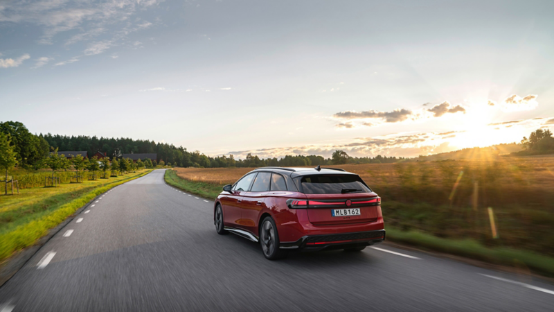 En röd Volkswagen kör längs en väg i solnedgången