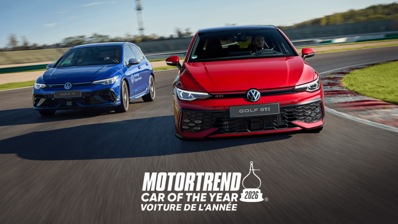 Une Volkswagen Golf GTI rouge mène une Volkswagen Golf R bleue sur une piste de course sous un ciel bleu clair.