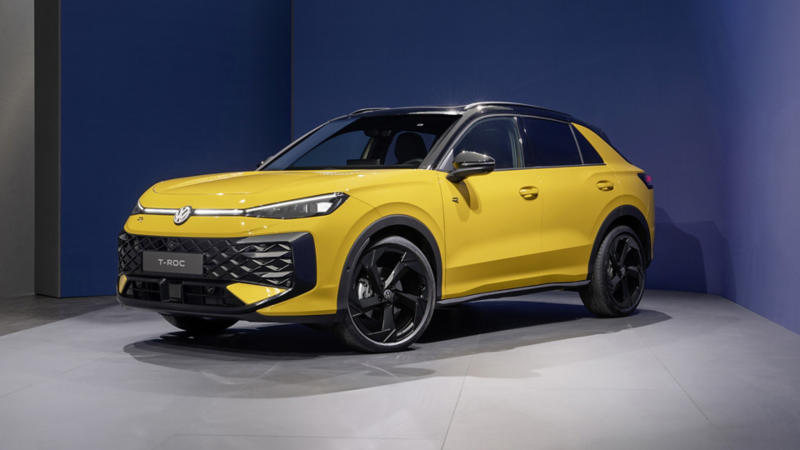 En gul T-Roc sedd snett framifrån, parkerad i en studio med blå väggar i bakgrunden