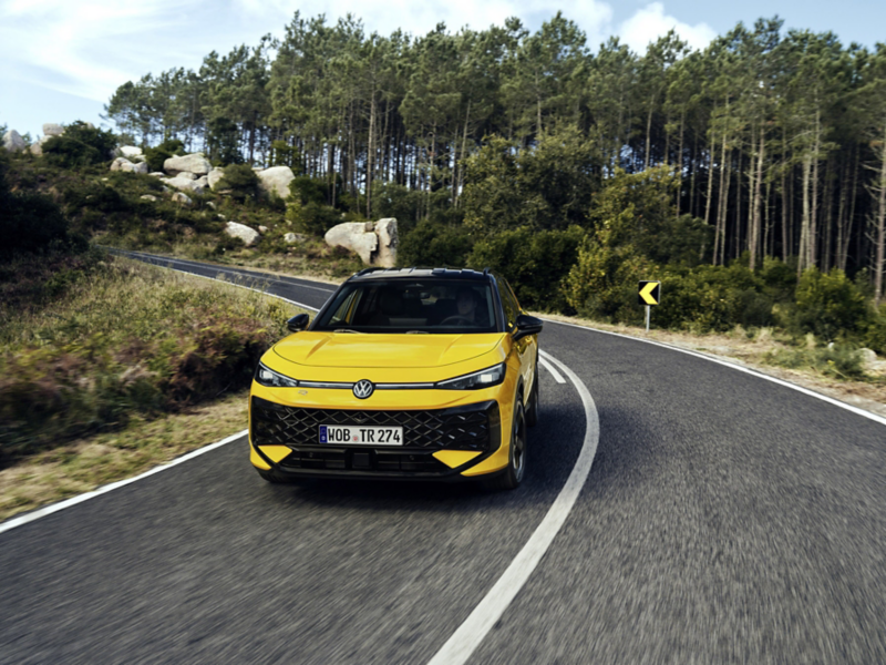 En gul VW T-Roc kör längs väg kantad av skog