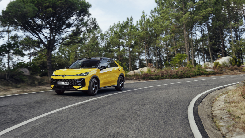 En gul T-Roc kör längs en kurvig väg kantad av skog